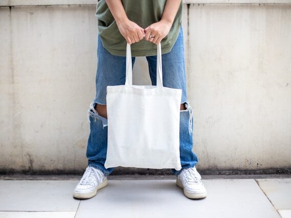 Tシャツに膝が破れてデニムをはいている男性が両手で白いトートバッグを持っている画像