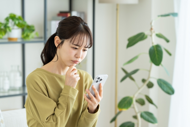 スマホを持って悩む女性の画像