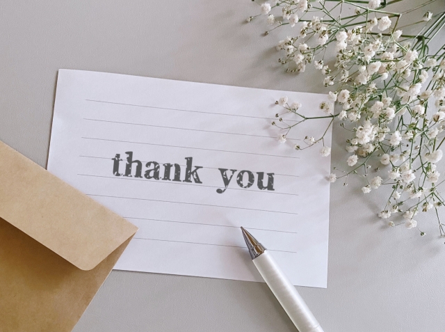 便箋に「thankyou」と書かれており、封筒とペンとカスミソウが周りにある画像