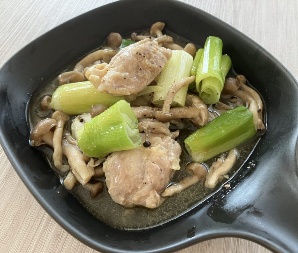 木目の台の上にある「鶏肉・白ネギ・キノコの和風アヒージョ」の画像