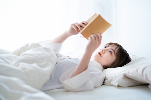 女性がベッドでリラックスして本を読んでいる画像
